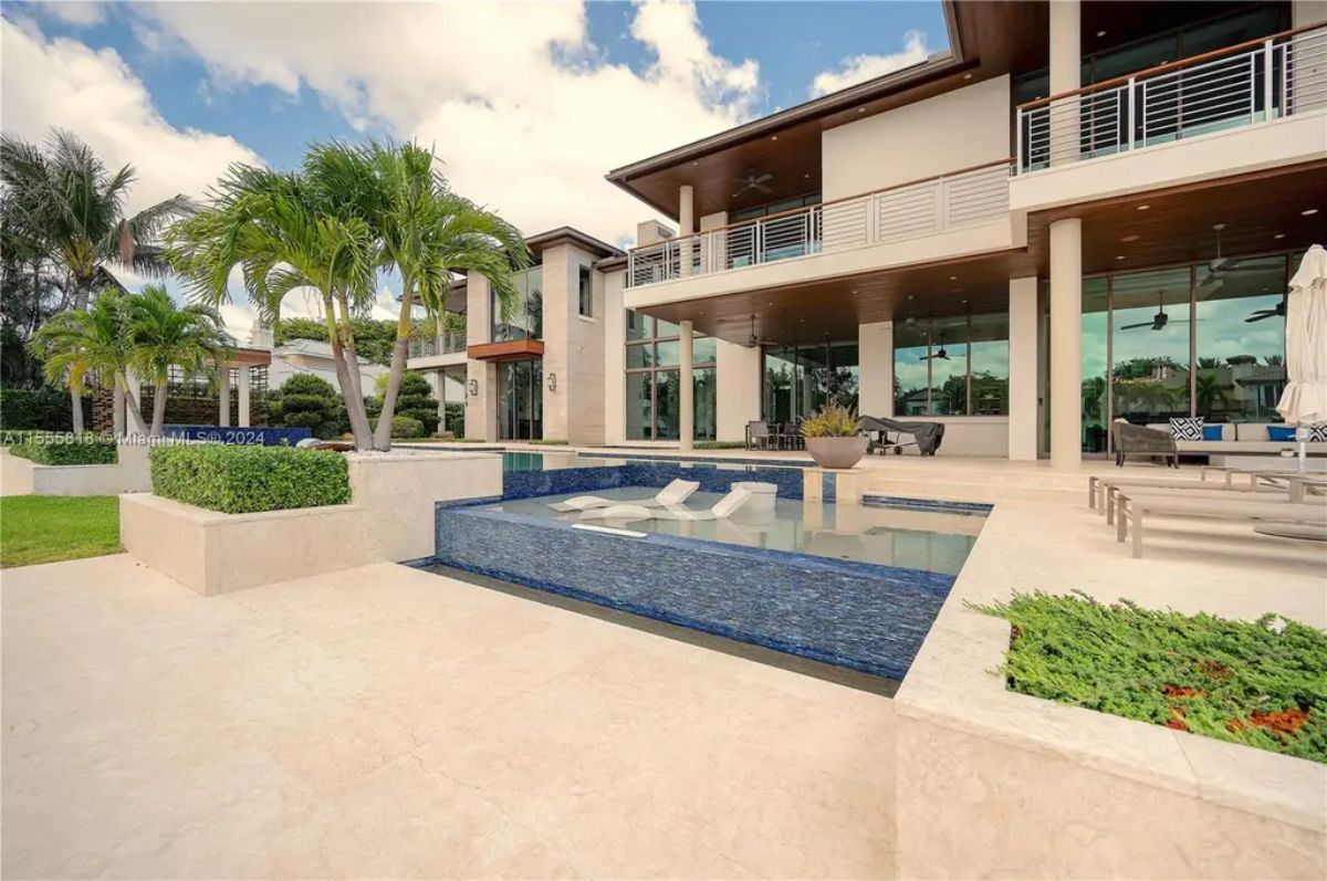 A resort-style pool with built-in lounge chairs, surrounded by lush greenery and modern architecture, enhances the backyard oasis. 