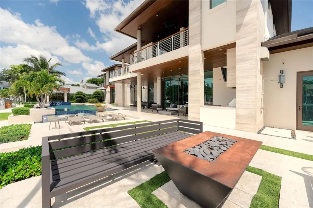 A stylish outdoor fire pit area is surrounded by sleek benches and lush landscaping, creating a perfect spot for evening gatherings. 