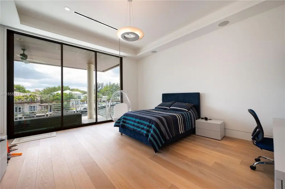 A sleek bedroom with a dark blue bed frame, a minimalist design, and access to a balcony overlooking a serene canal. 