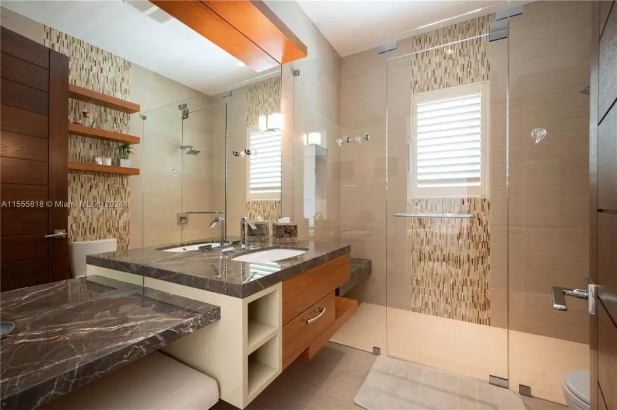 A contemporary bathroom combines warm wood tones, marble countertops, and a glass-enclosed shower with accent tiles. 