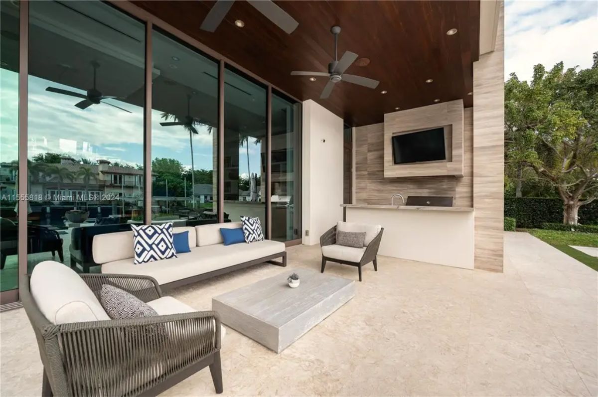 An elegant outdoor lounge features a covered seating area, a ceiling fan, and a built-in bar with a wall-mounted TV. 