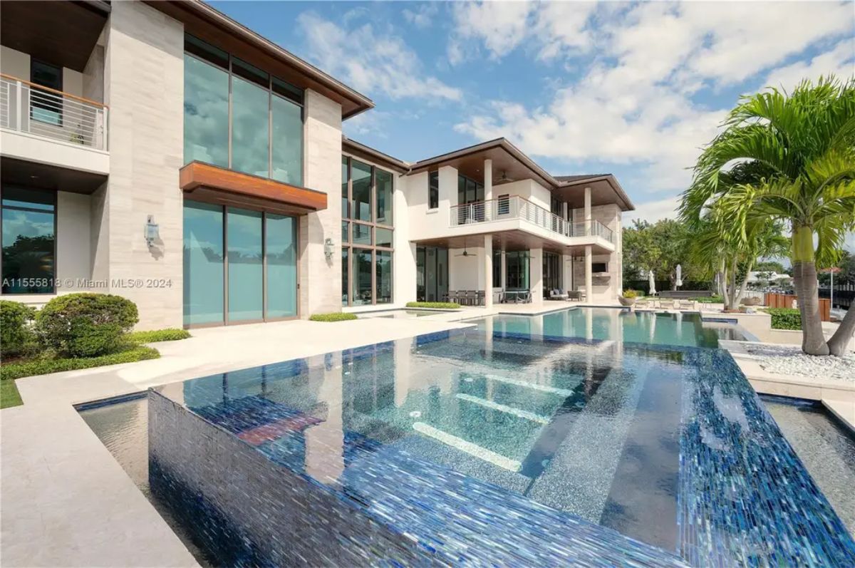 An infinity-edge pool with shimmering blue tiles reflects the grandeur of the waterfront mansion. 
