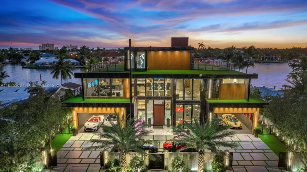 Three-story contemporary home features floor-to-ceiling glass windows, wood paneling, and artificial green turf accents.