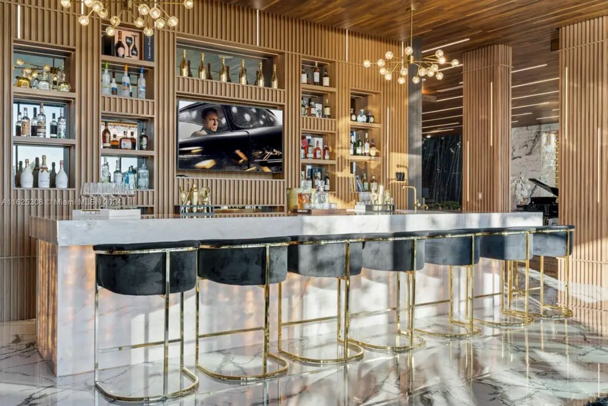 Long marble bar with gold fixtures is paired with black velvet stools featuring gold frames.