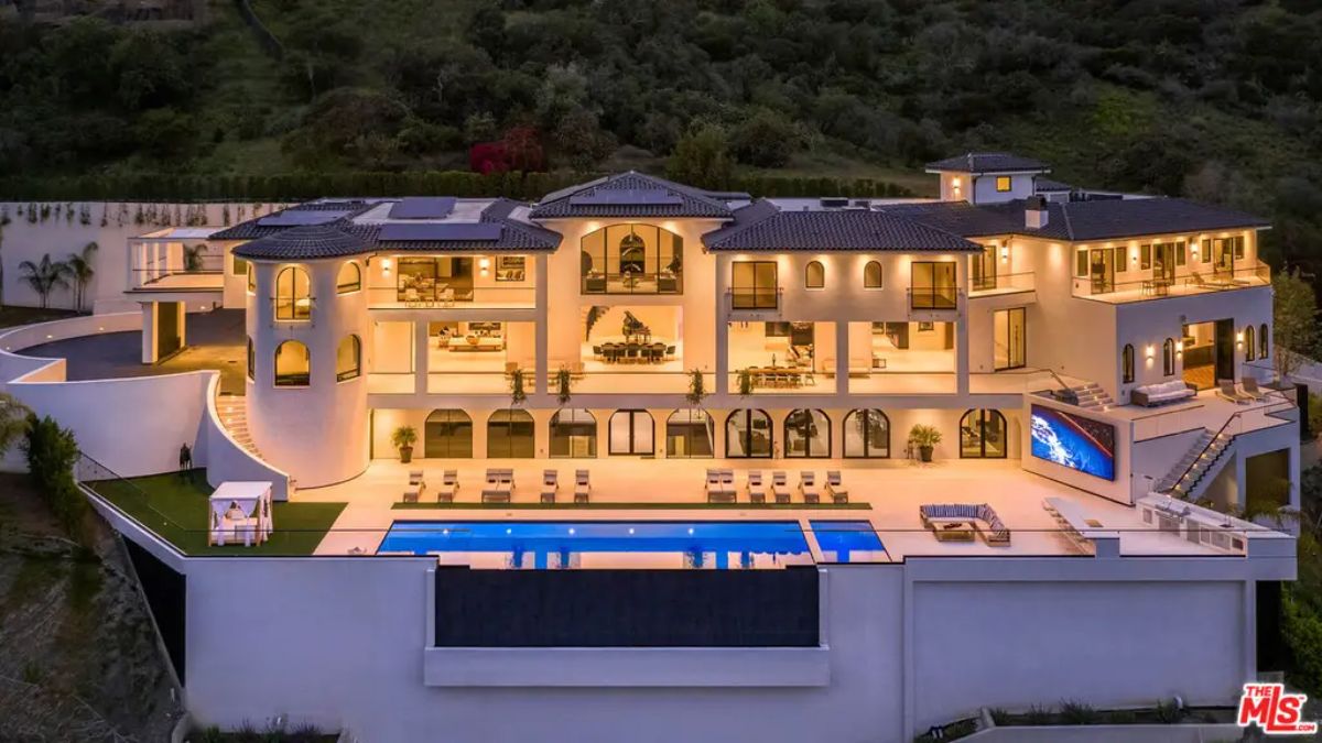 Grand villa features an expansive terrace with an infinity pool, lounge chairs, and large glass windows revealing luxurious interiors. 