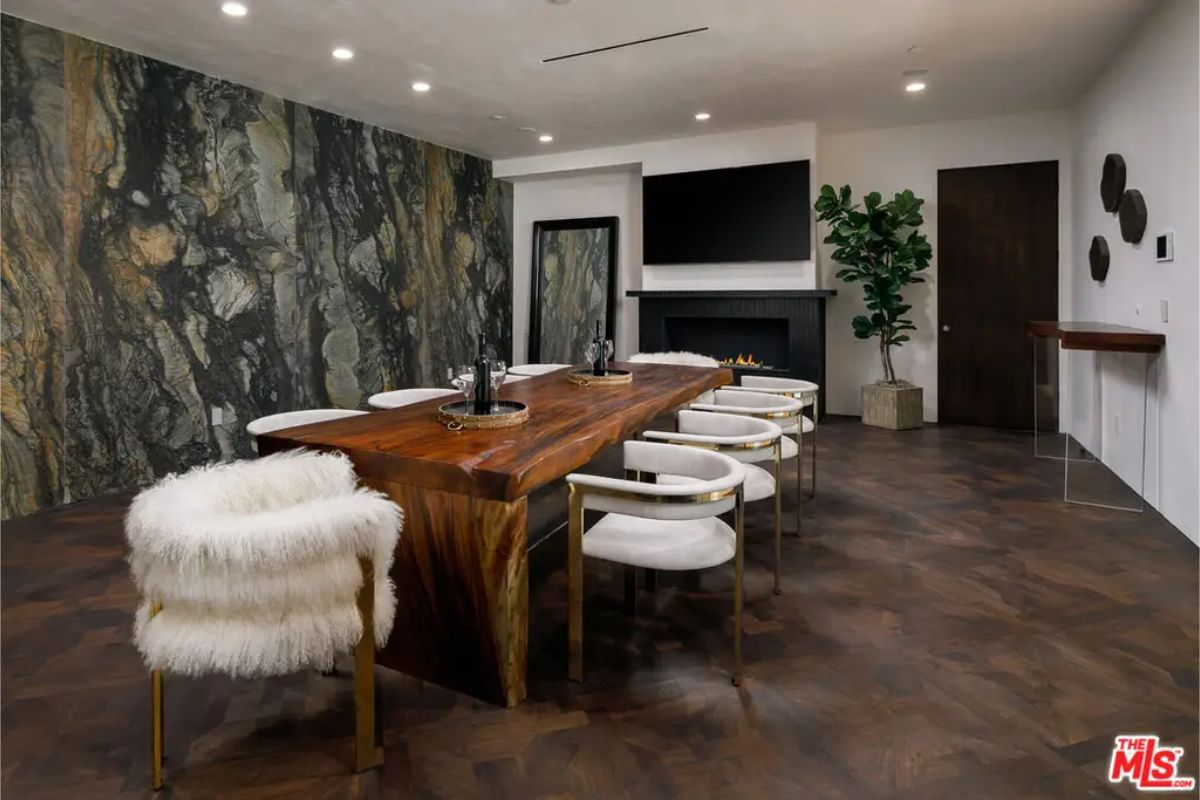 Unique dining room centers around a live-edge wooden table surrounded by plush white chairs, with a dramatic stone accent wall. 