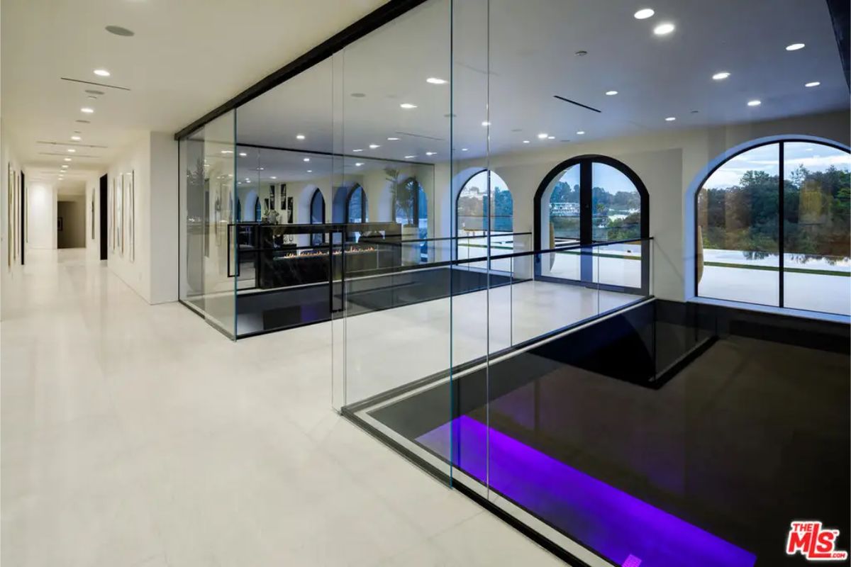 Modern hallway with glass walls and large arched windows offering natural light and a view of the outdoors. 