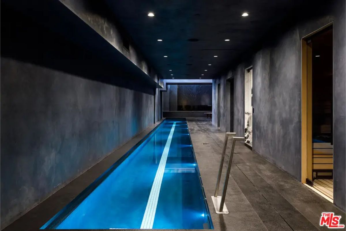 Indoor lap pool illuminated with blue lights, surrounded by dark-toned walls creating a sleek ambiance. 