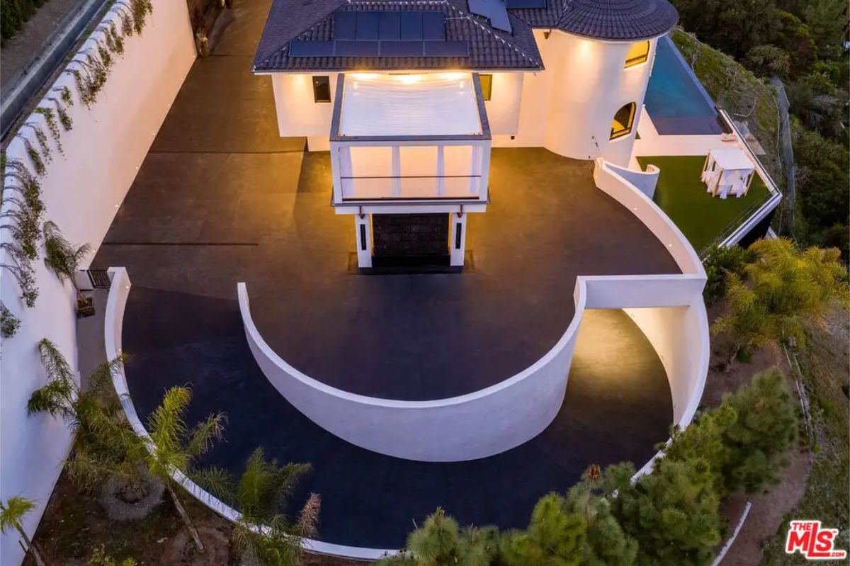 Circular driveway leading to the modern entrance of the mansion, highlighted by warm exterior lighting and surrounded by greenery. 