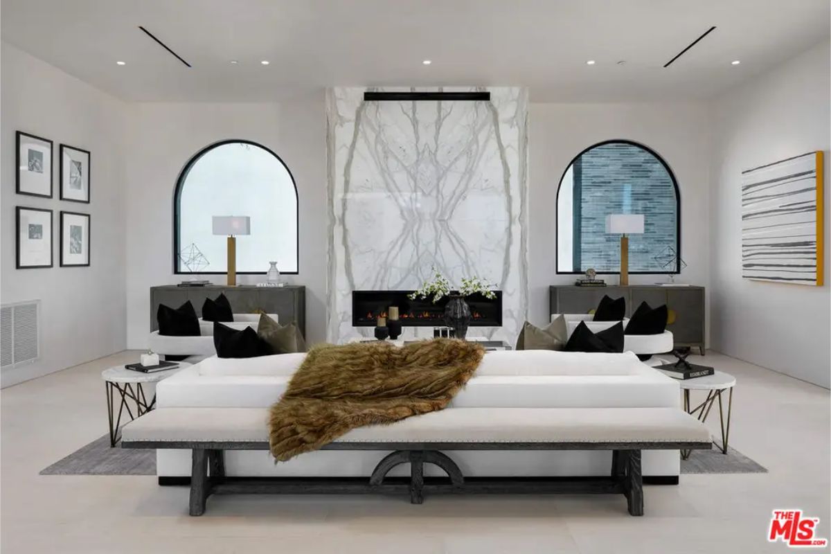 Sophisticated sitting area highlights a marble-accented fireplace, contemporary white sofa, and symmetrical arched windows that enhance natural light. 