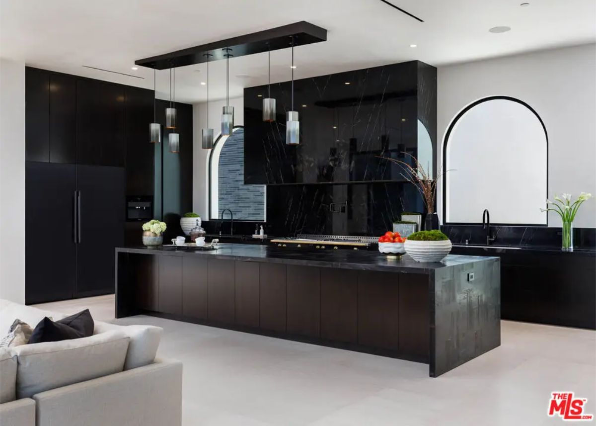 Sleek kitchen design features black cabinetry, a large central island, and pendant lighting, complemented by arched windows for architectural interest. 