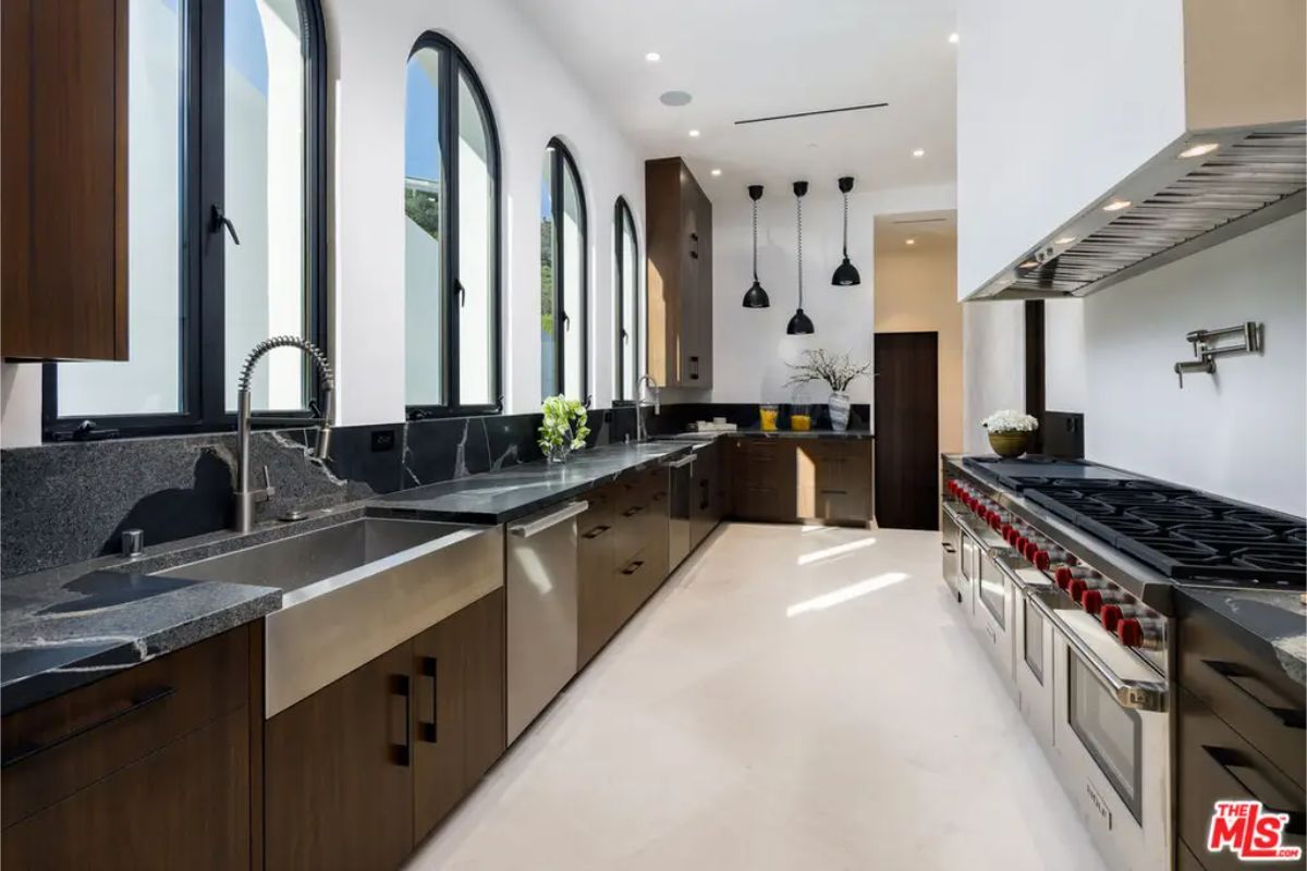 Gourmet kitchen is equipped with high-end stainless steel appliances, black stone countertops, and tall arched windows allowing natural light to flood the space. 