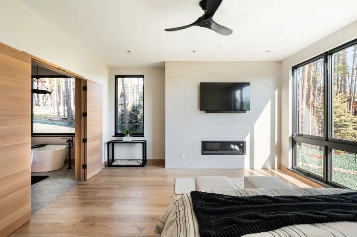 Luxurious bedroom suite with a fireplace, ceiling fan, and expansive window views. 