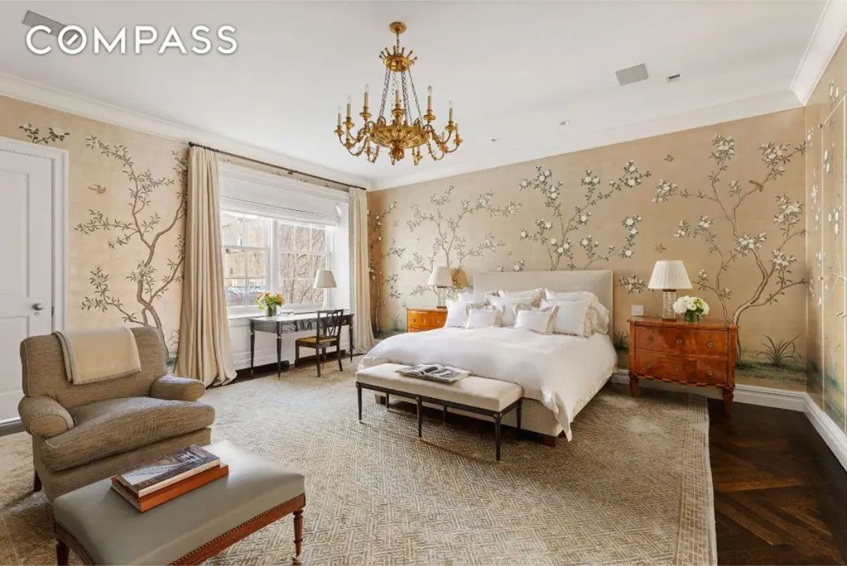 Large bedroom with floral-patterned wallpaper and a gold chandelier.