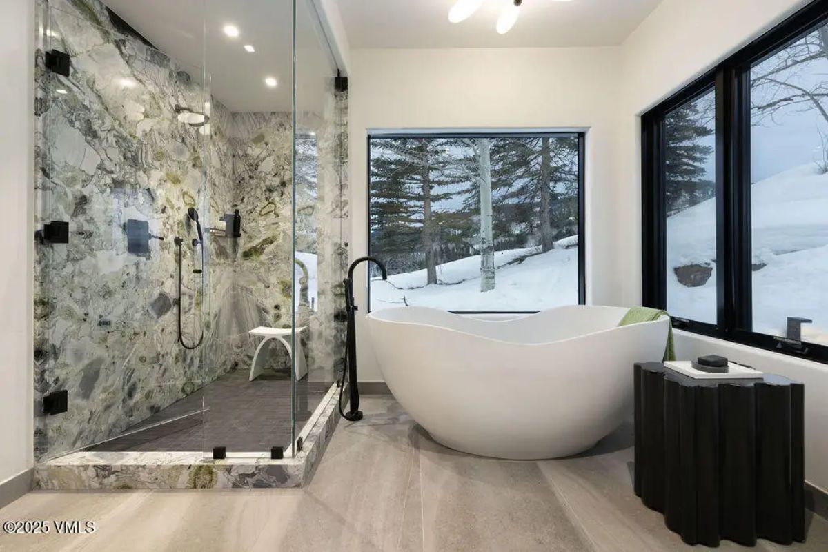 A freestanding sculptural bathtub positioned beside large windows showcasing snowy outdoor scenery.