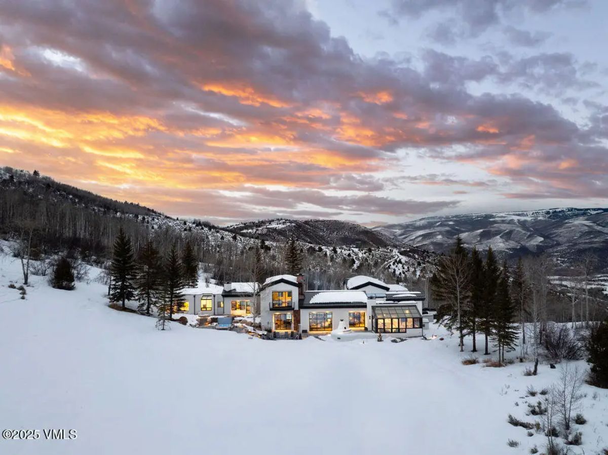 Contemporary residence nestled in a snow-covered valley surrounded by mountain ranges and dense forest.