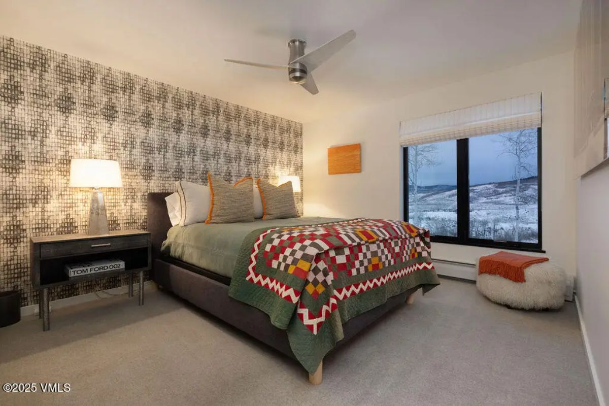 A bold geometric accent wall, soft neutral carpeting, and a large window showcasing snow-covered mountain scenery.