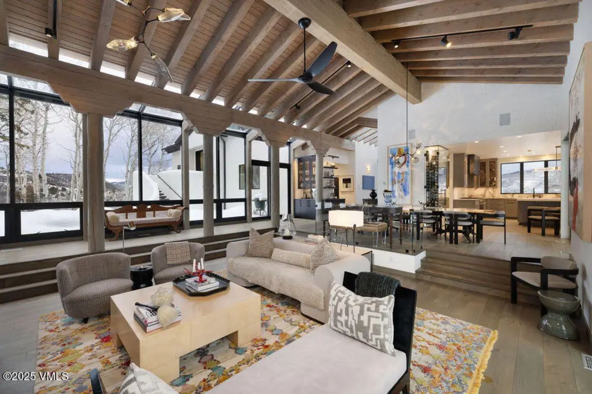 Expansive living area with vaulted wooden ceilings, exposed beams, and floor-to-ceiling windows offering mountain and forest views.