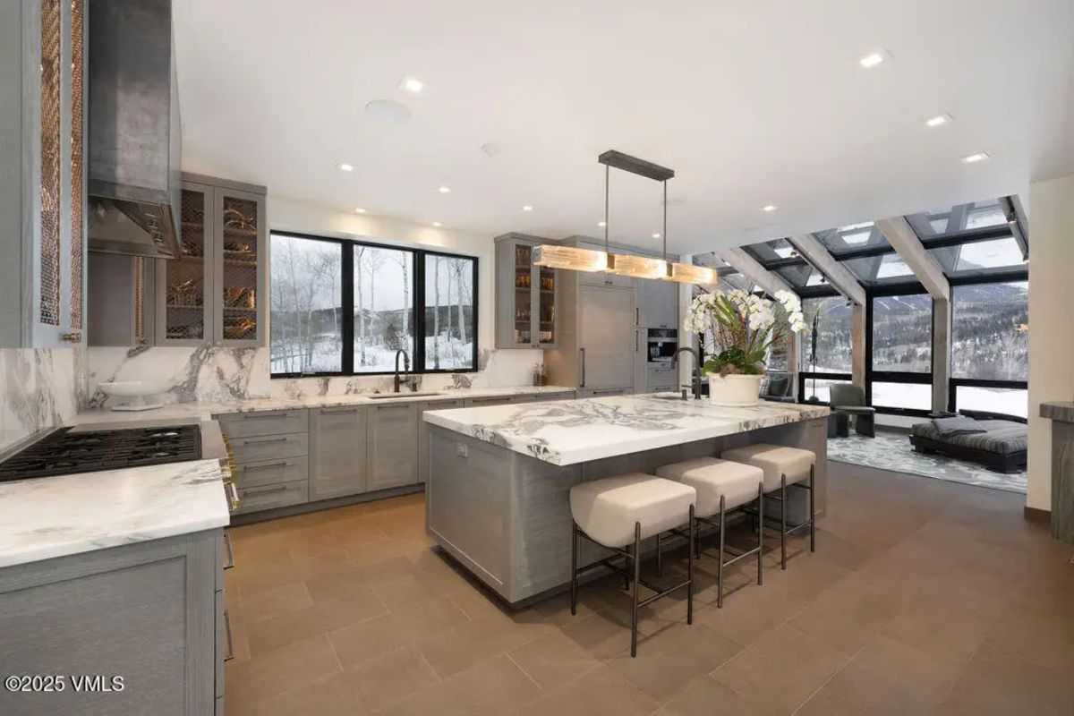Open-concept kitchen with sleek gray cabinetry, marble countertops, and a large center island with seating for three.