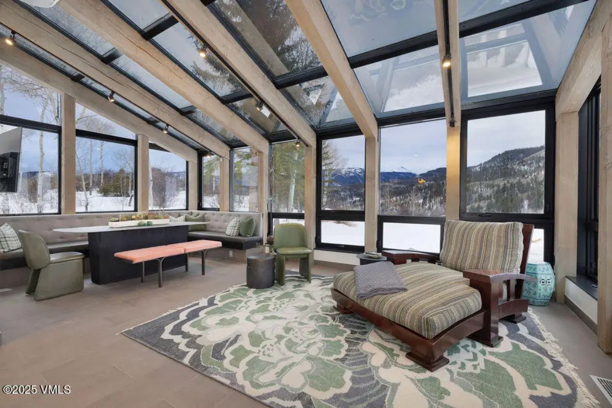 Glass-enclosed sunroom with vaulted ceilings, exposed wooden beams, and floor-to-ceiling windows.
