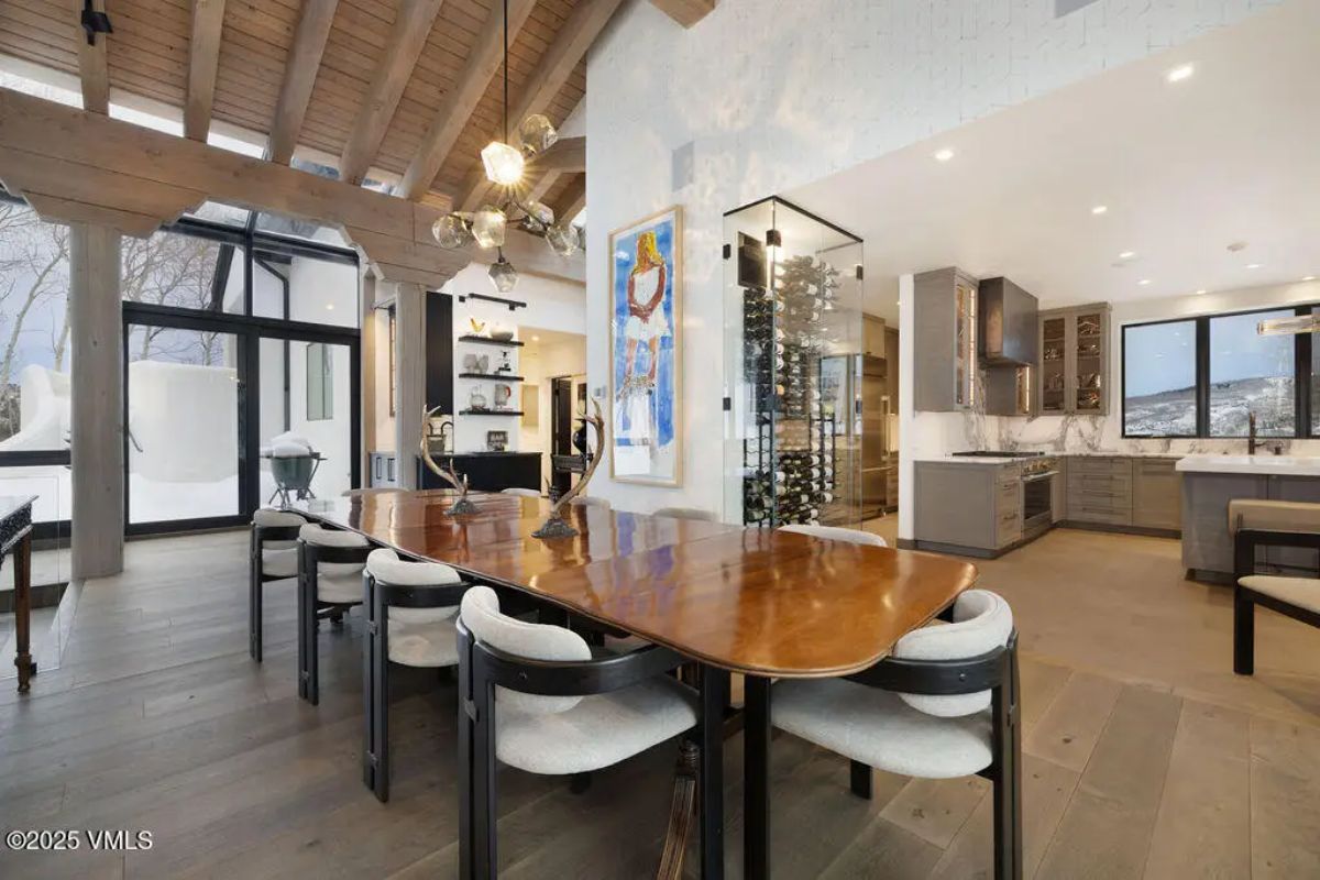 Polished wood dining table with seating for eight, set beneath an artistic chandelier and vaulted wood-beamed ceiling.