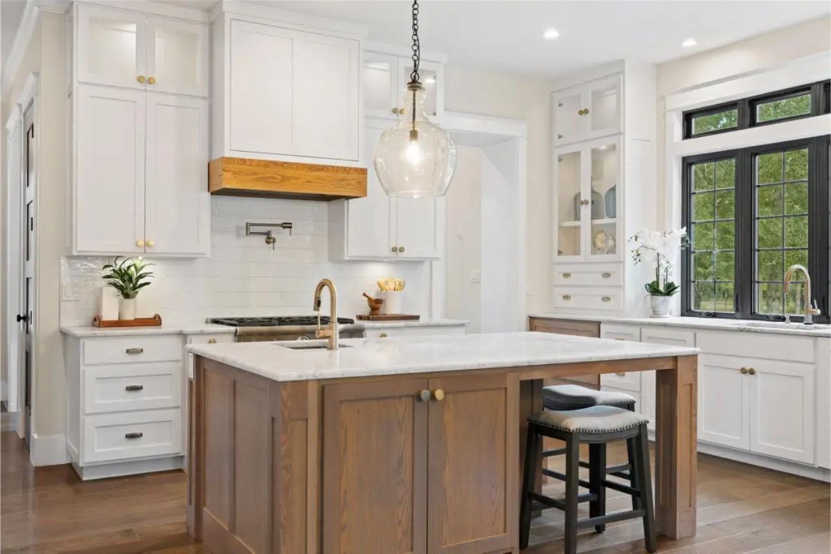White cabinetry, gold hardware, and a large central island with a wood base and marble countertop.