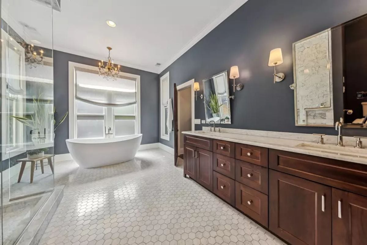 White freestanding bathtub is positioned in front of large windows with fabric Roman shades.