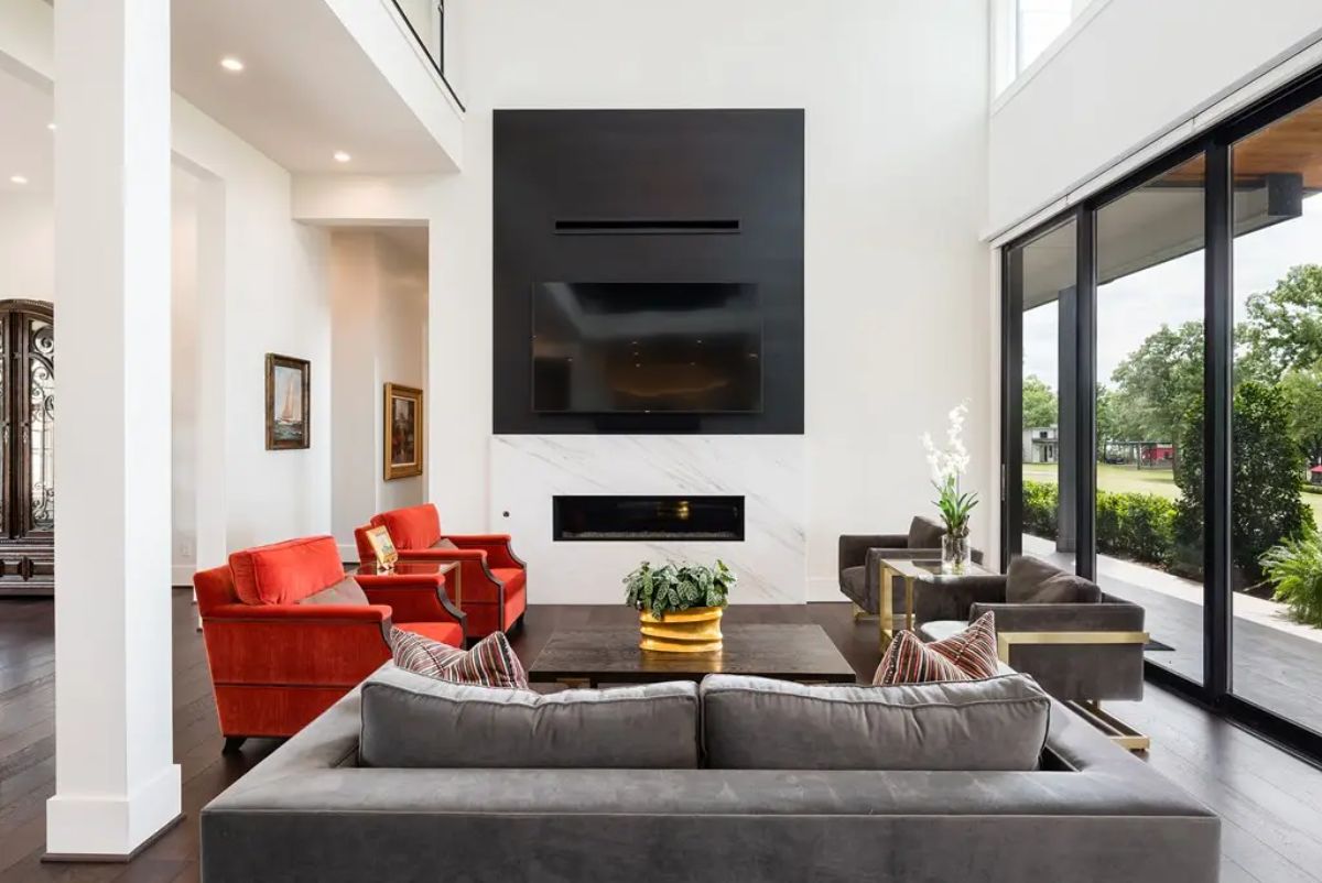 Large living room with high ceilings, dark wood flooring, and a black accent wall surrounding a fireplace and mounted television.
