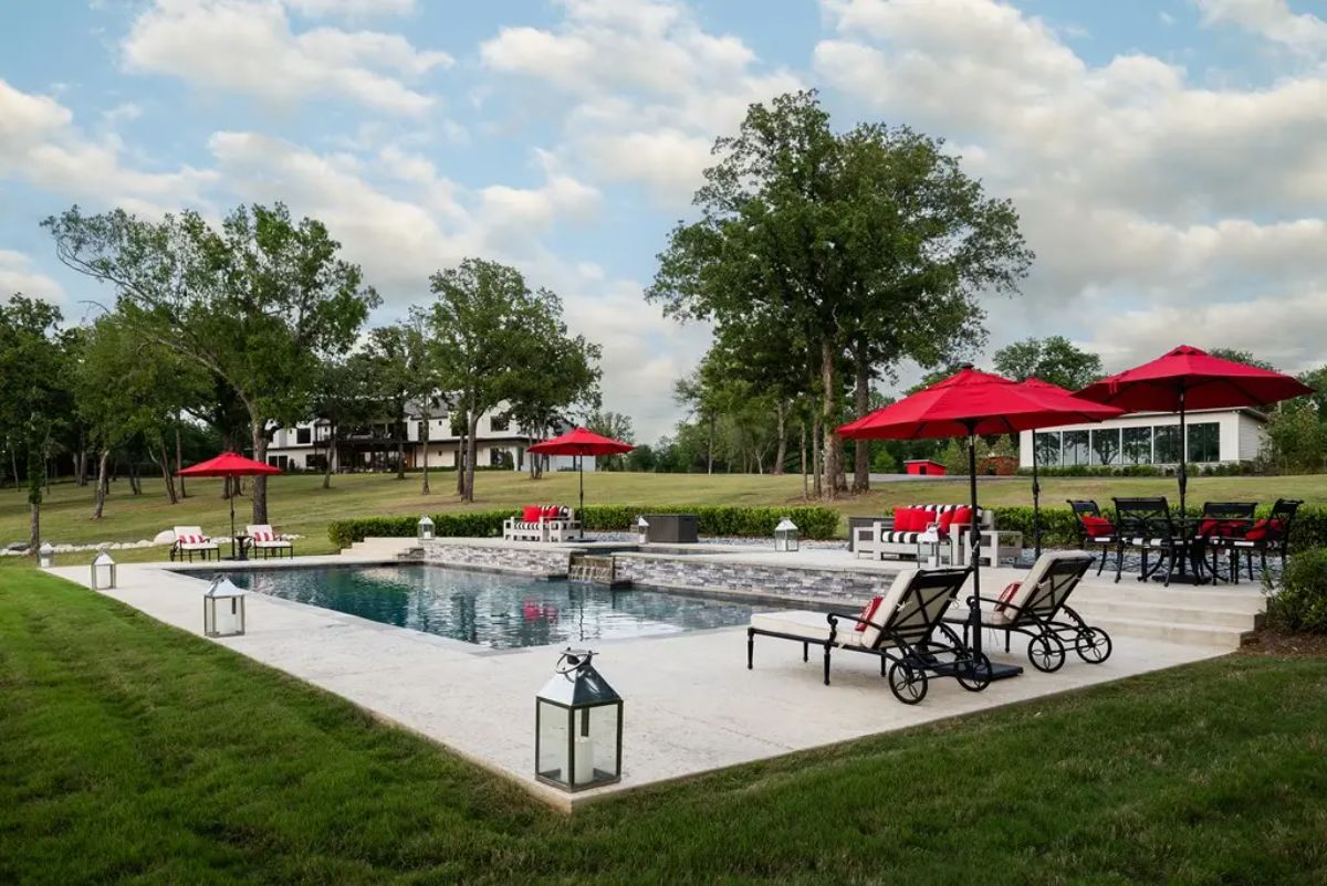 Swimming pool surrounded by lounge chairs, seating areas, and red patio umbrellas.