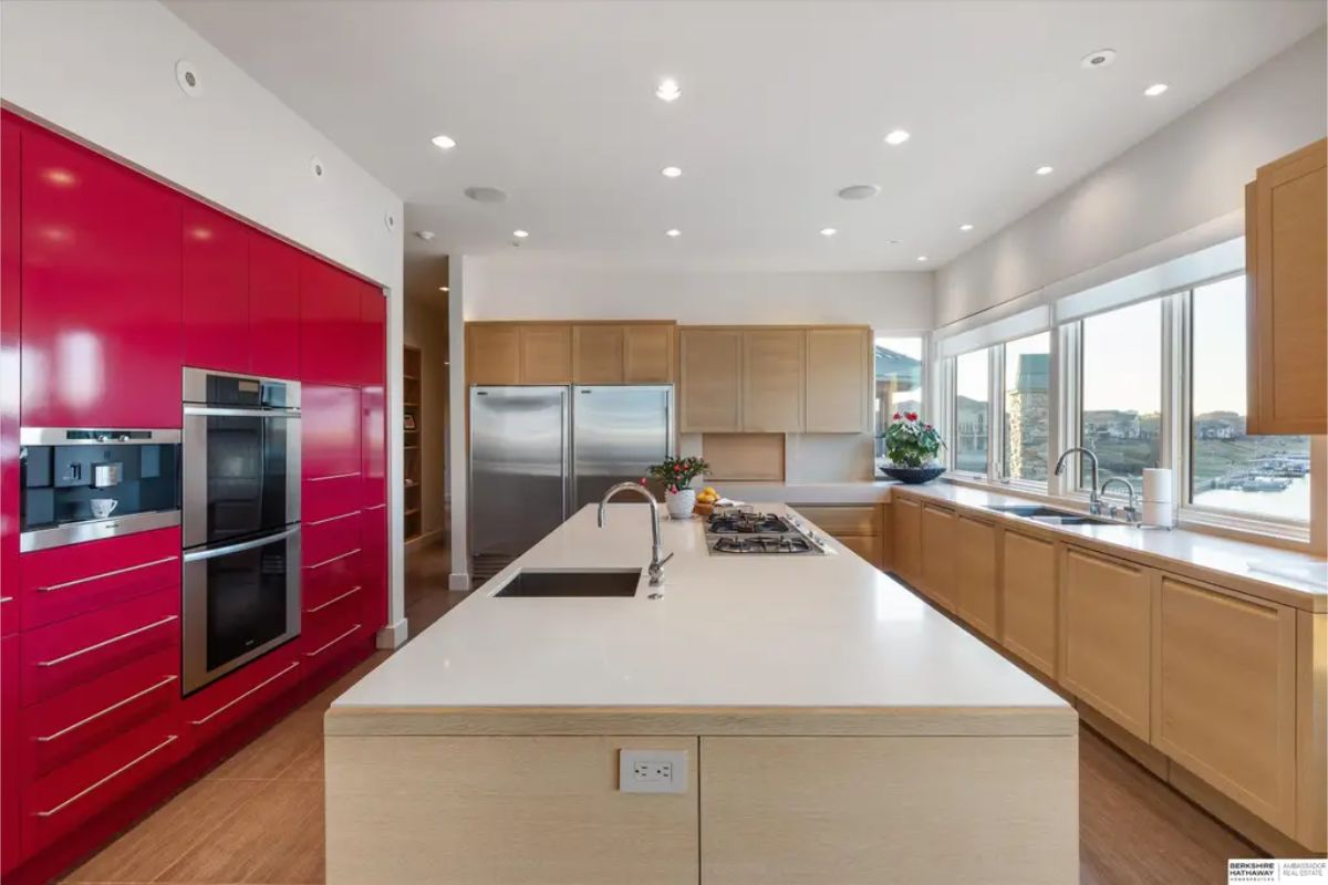 Modern kitchen with a bold red accent wall, stainless steel appliances, and a large island with a white countertop. 