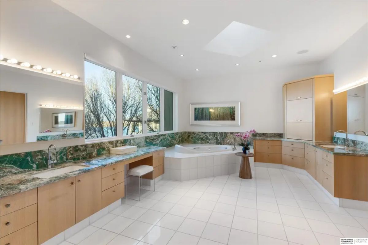 Expansive bathroom with dual vanities, green marble countertops, a soaking tub, and a skylight. 