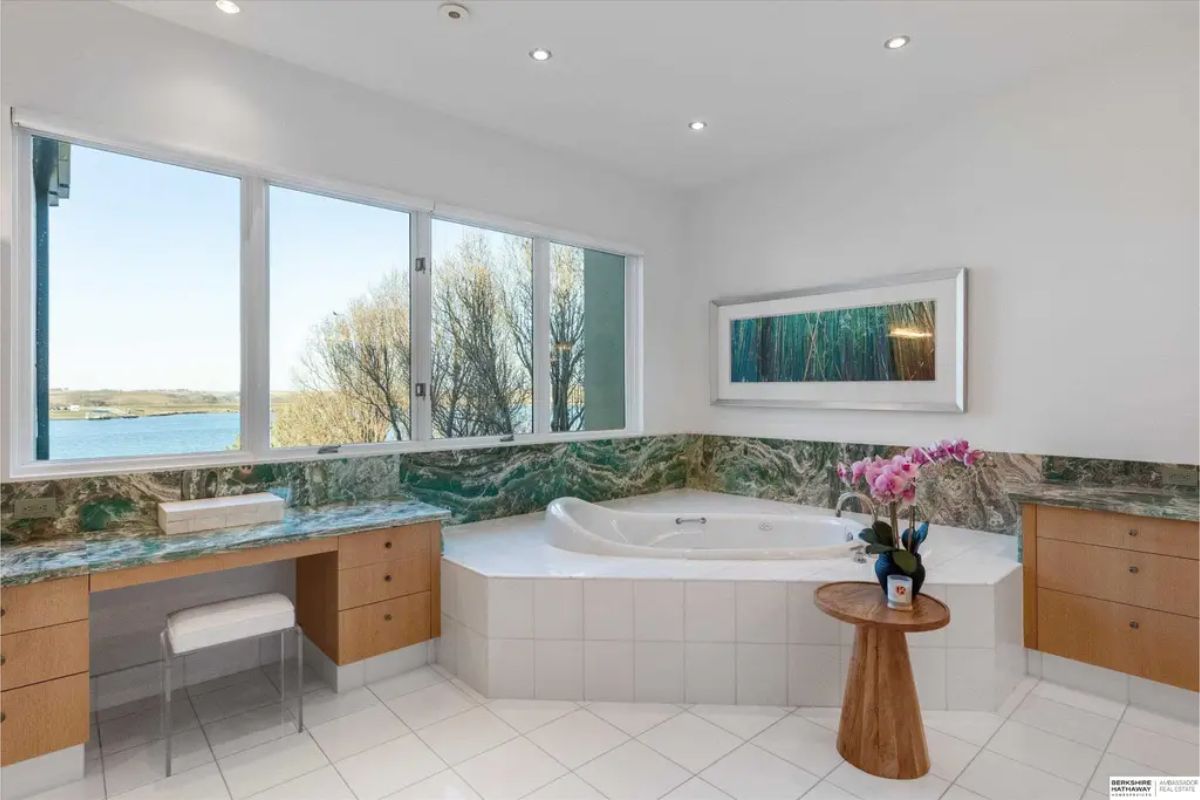 Close-up of a soaking tub complemented by a green marble backsplash and large windows providing a scenic outdoor view. 