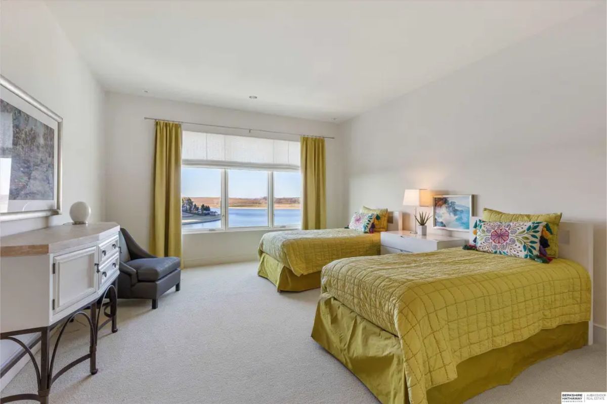 Bright bedroom showcasing twin beds with mustard-colored bedding and a large window overlooking a serene lake. 