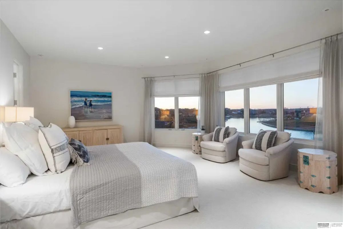 Spacious bedroom with a king-size bed, soft neutral tones, and large windows offering a picturesque waterfront view. 