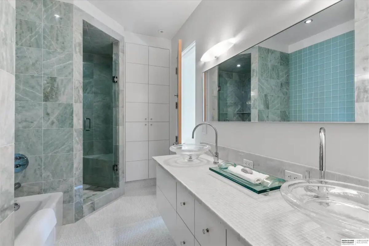 Sleek bathroom incorporating glass sinks, a marble shower, and a modern aesthetic. 