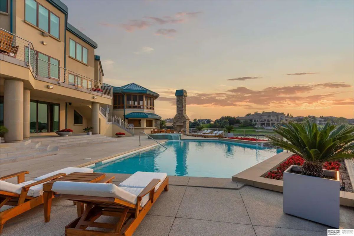 Luxurious poolside lounge area features plush sunbeds, a lush potted plant, and a serene sunset over a calm body of water. 