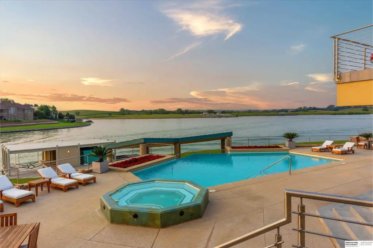 Stunning outdoor pool area with a spa, lounge chairs, and a tranquil lake in the background during sunset. 