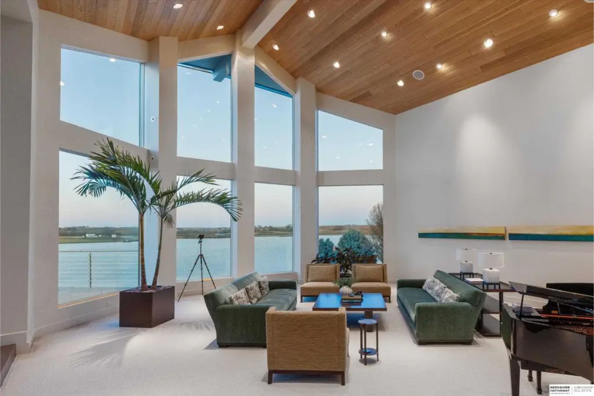 Another angle of the living room highlighting its towering wooden ceiling, a grand fireplace, and stylish contemporary furnishings in earthy tones. 