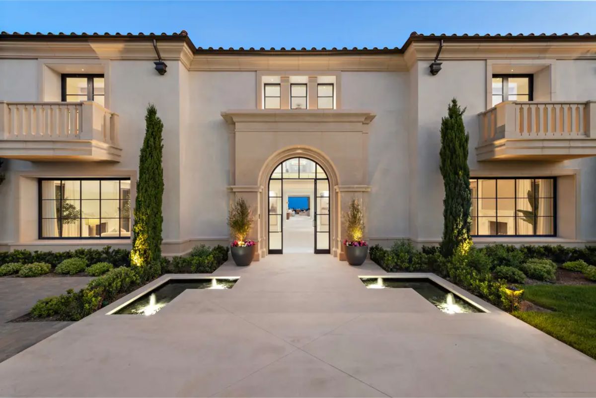 Grand entrance features an arched doorway, elegant stonework, and lush greenery leading into the home. 