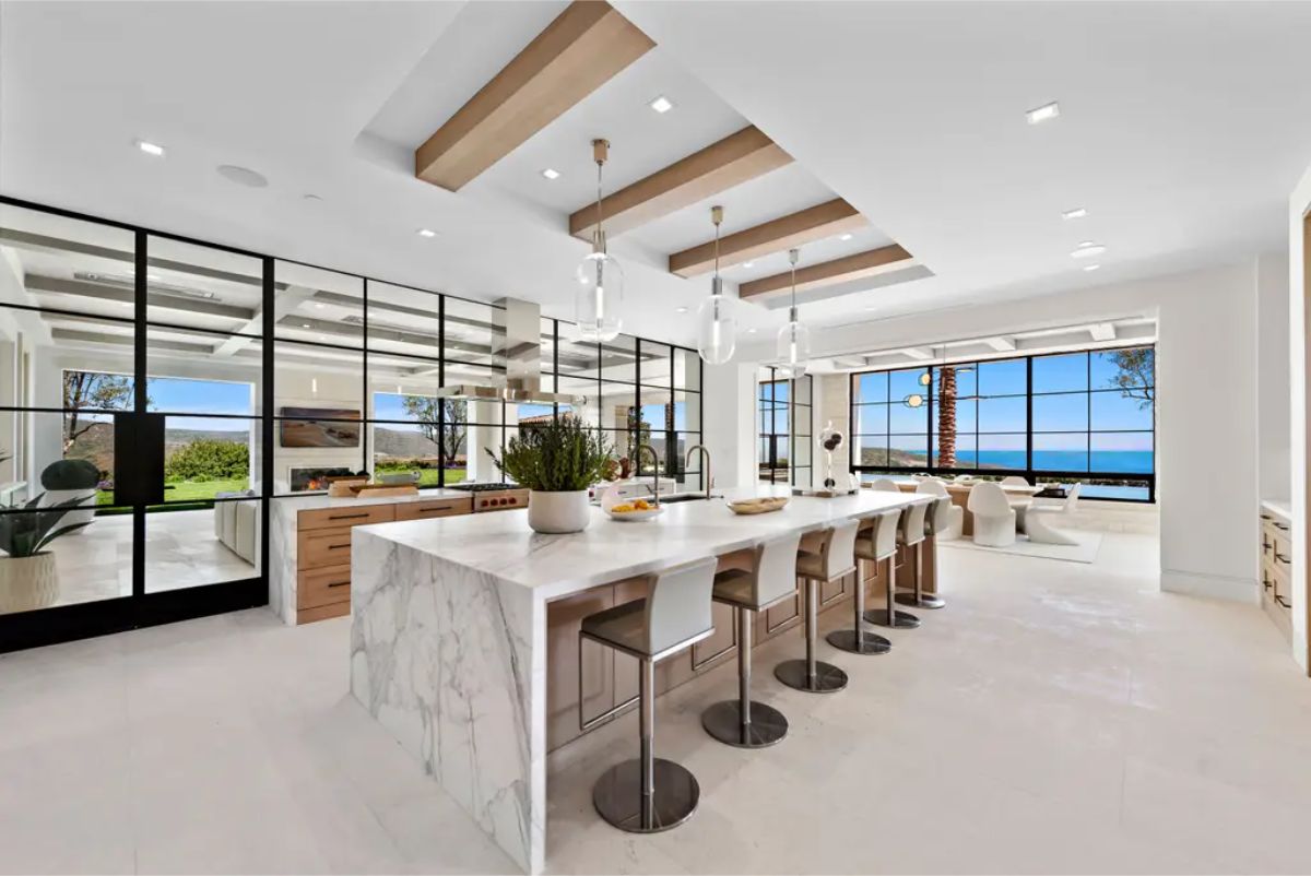 Gourmet kitchen combines wood, marble, and floor-to-ceiling glass panels, offering a seamless view of the ocean. 
