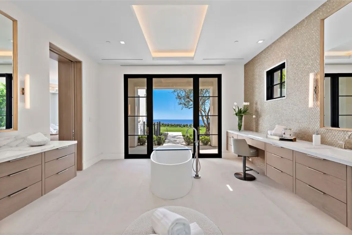 Elegant bathroom featuring a freestanding tub, vanity area, and access to an outdoor garden with ocean views. 