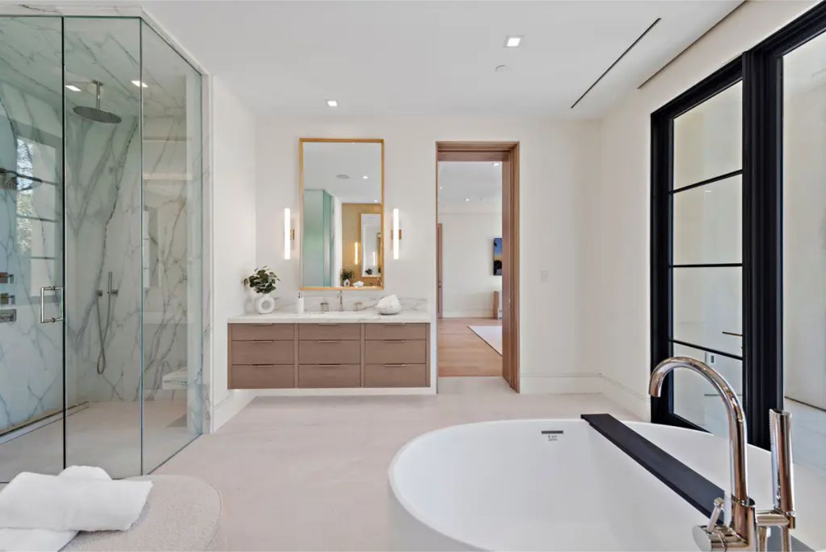 Modern bathroom with a glass-enclosed shower, dual vanity, and a freestanding bathtub. 
