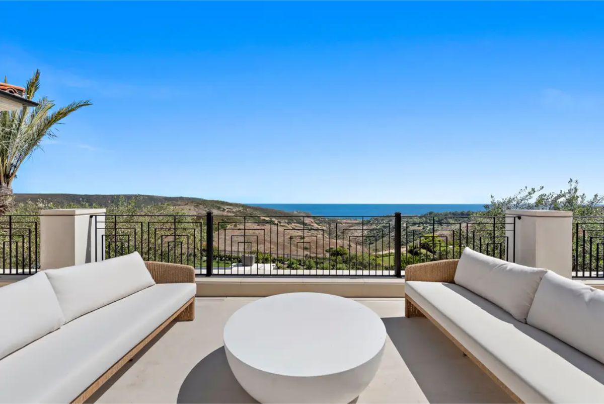 Private balcony with cushioned seating, offering panoramic views of the hills and ocean. 