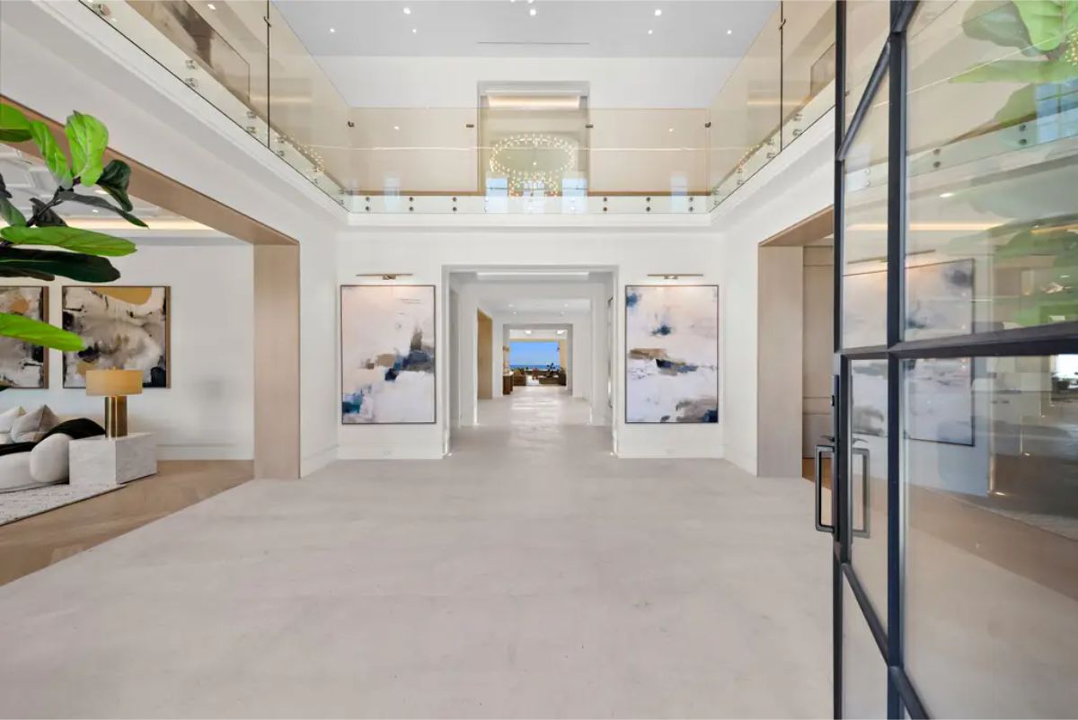 Spacious foyer showcases high ceilings, modern glass railings, and a long hallway with distant ocean views. 