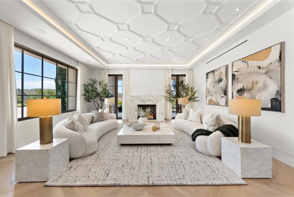 Stylish living room is furnished with curved sofas, contemporary art, and a geometric ceiling design. 