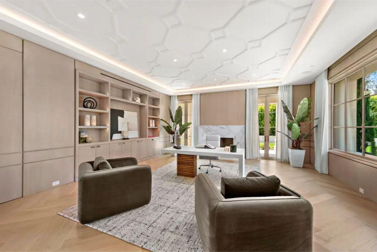 Sophisticated home office is adorned with built-in wooden shelves, a sleek fireplace, and plush seating. 