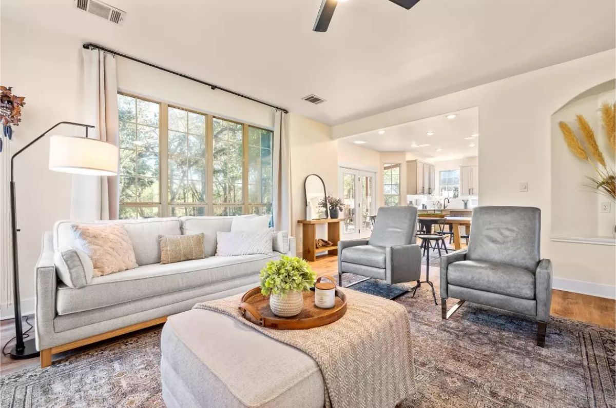 Living room with large windows, neutral-toned furniture, and a mix of modern and classic decor.