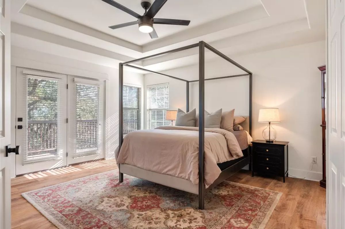 Bedroom with a metal-frame canopy bed, beige bedding, and a large patterned area rug.