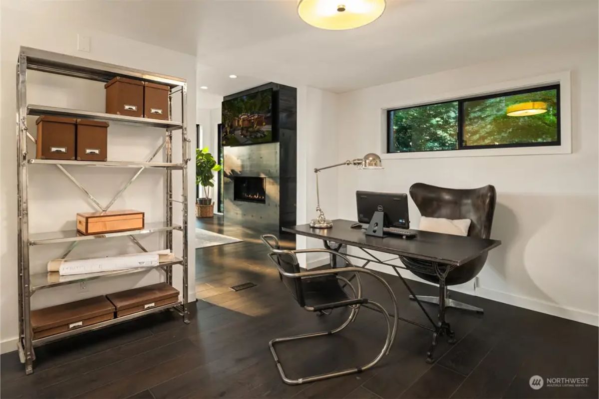 Minimalist home office featuring a black metal desk, an industrial-style leather chair, and a metal shelving unit with storage boxes. 