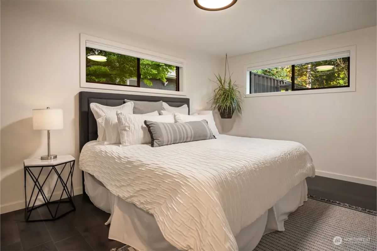 Cozy bedroom with a plush white bed, black and white decor, and large windows bringing in natural light. 